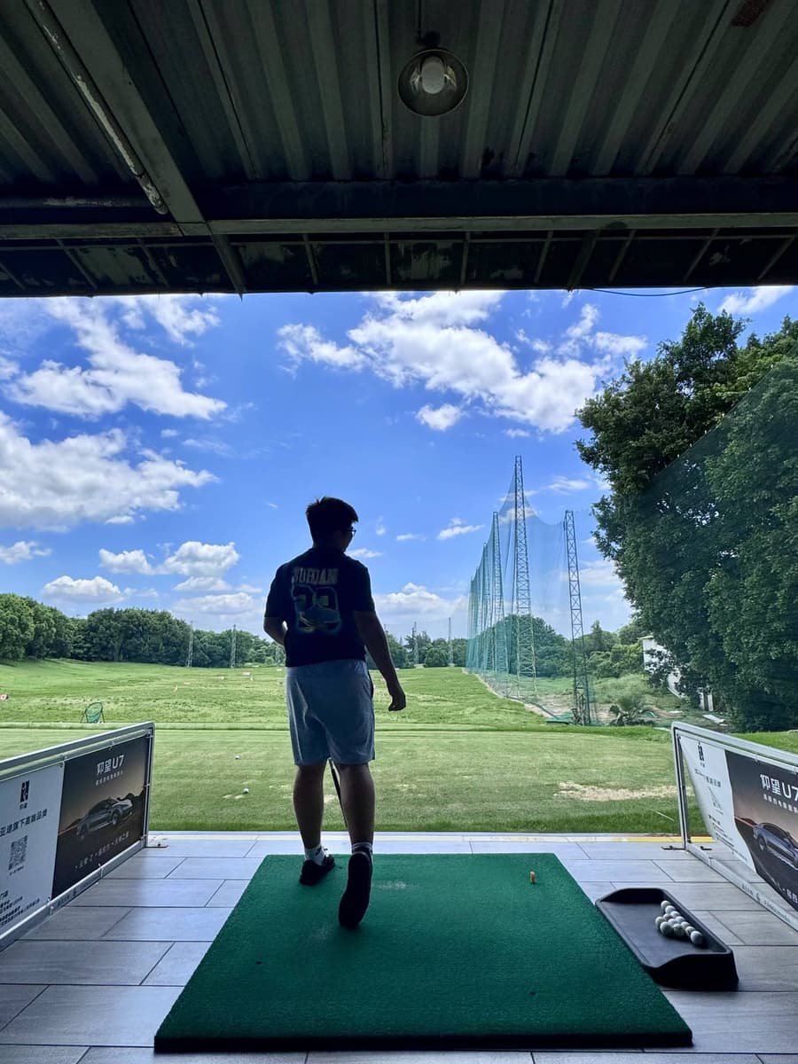 Yuzhe holding a golf club at an outdoor driving range, seen from behind.