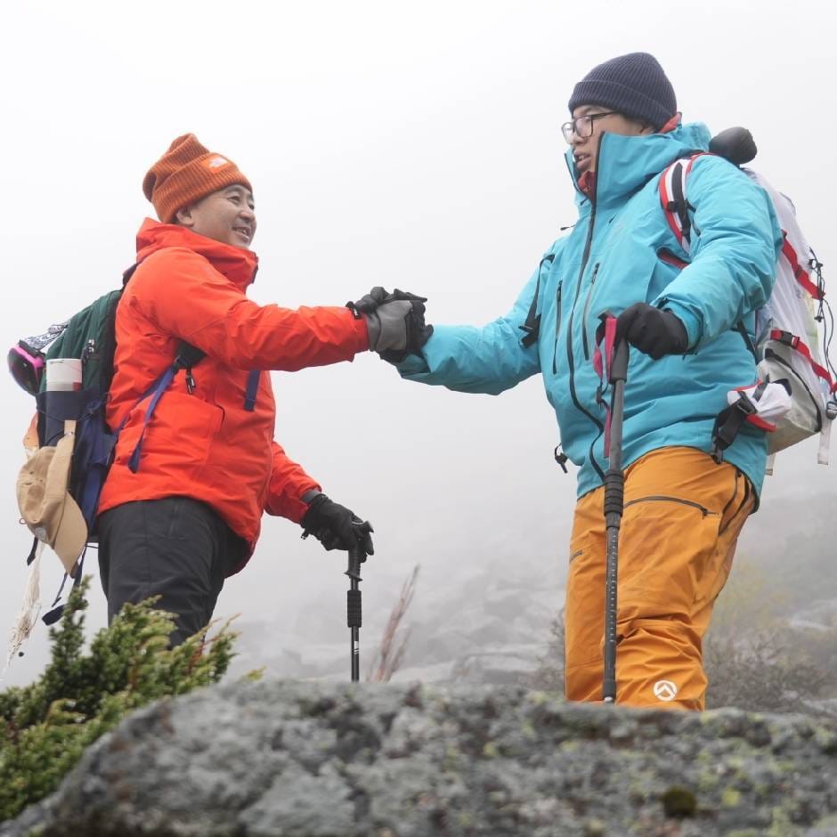 Yuzhe, on the right in a blue jacket and yellow trousers, holding hands with his father, on the left in an orange jacket, on a misty hike.