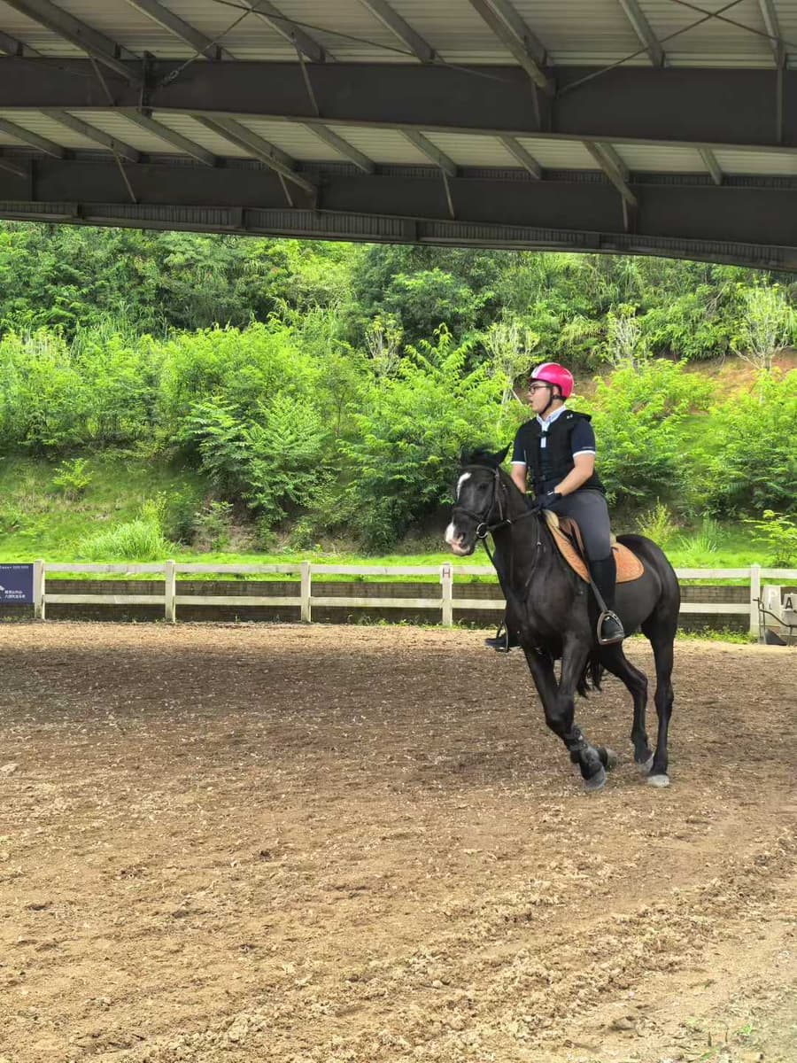 Yuzhe riding a black horse in an arena, wearing a helmet and riding vest.